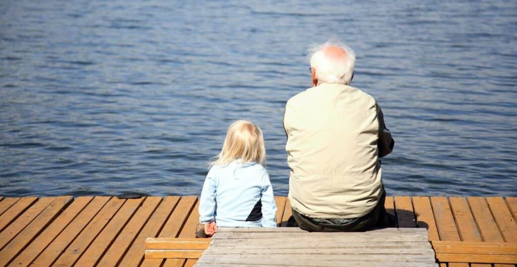 Grandad and granddaughter sat on a lake jetty